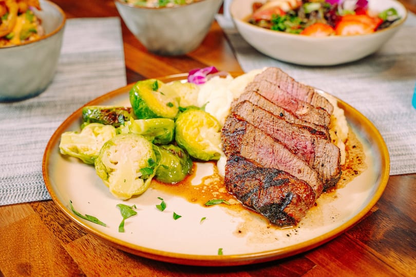 Sliced steak with mashed potatoes and roasted Brussels sprouts on a plate.