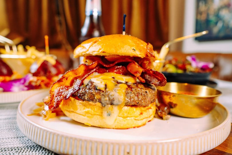 Close-up of a juicy bacon cheeseburger with melted cheese and caramelized onions on a white plate.