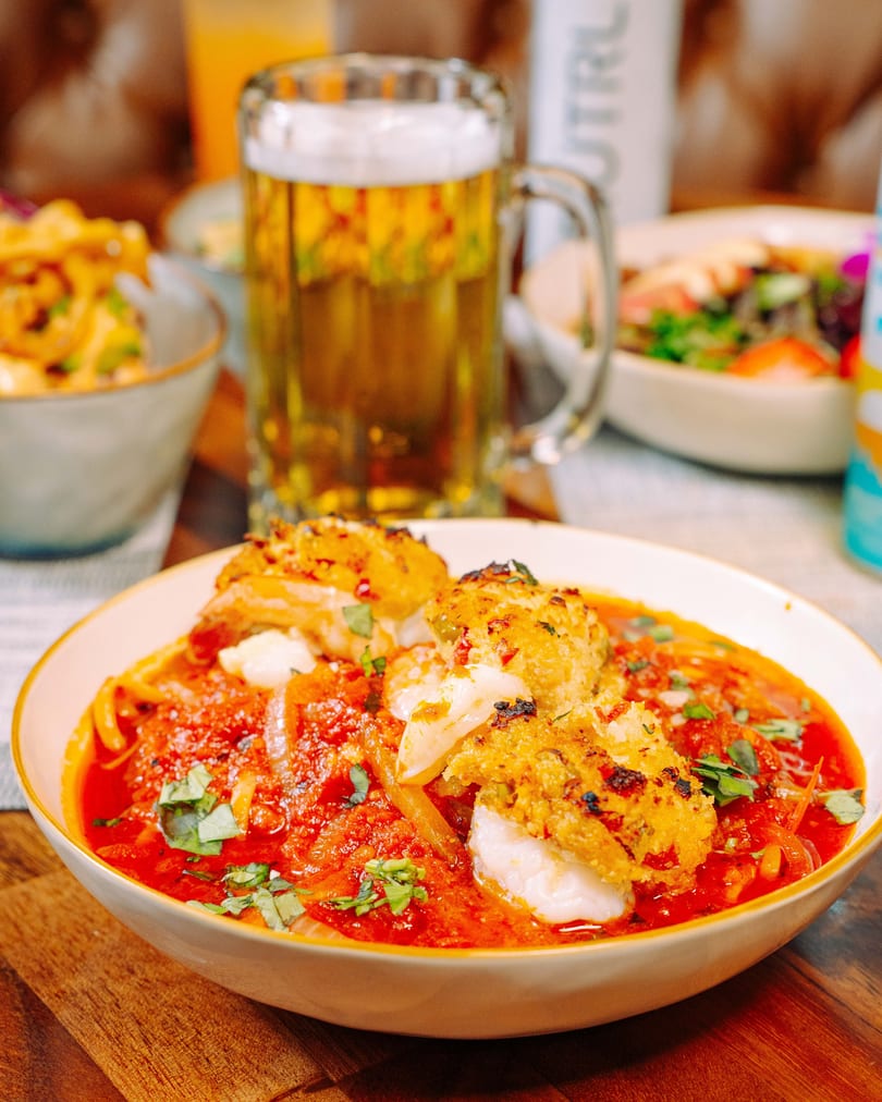 Seafood pasta with red sauce and basil, with a beer mug and salad in the background.